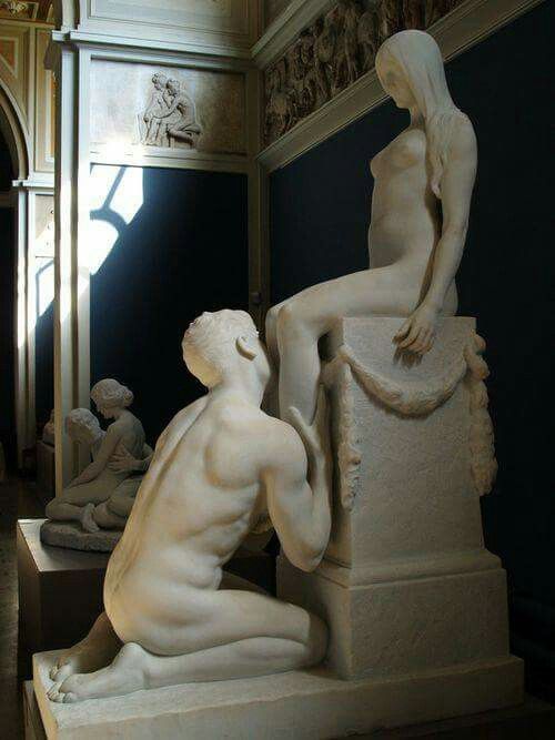 Sculpture of two lovers: man kneeling and touching feet of woman on pedestal. Both nude