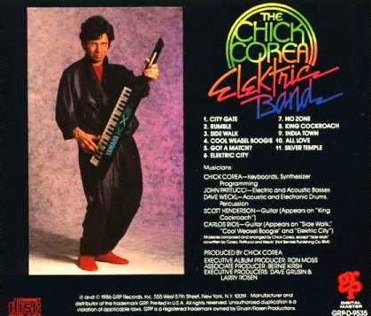 A page from a Chick Corea album booklet. It shows a standing Corea holding a small electronic keboard as if ready to play it, dressing in something that resembles a bath robe, along with red slippers. The rest of the image consists of a track listing, personnel information, and other data for the album.