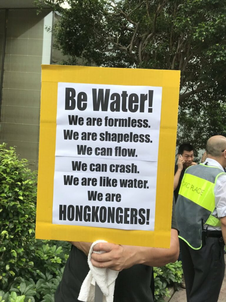 A Hong Konger holds up a sign that reads: "Be Water! We are formless. We are shapeless. We can flow. We can crash. We are like water. We are Hong Kongers!"