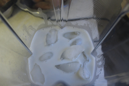 This is a photo looking down into a blender container from above. In the blender container is almond milk and ice, as per the recipe.