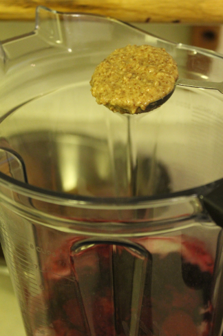 The photo shows a close-up of almond butter exiting a tablespoon and entering a blender container.