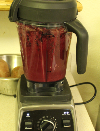 The photo shows the blender with the lid atop the container. It is blending the completed smoothie, which is a very purple-dark color.