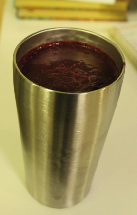 The image shows a metal cup containing a beet root smoothie (which is dark purple). The metal cup is standing on a countertop.