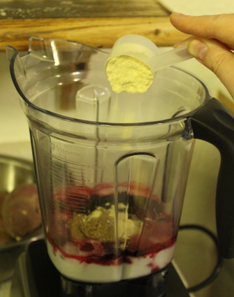 The photo shows a scoop of pea protein powder being poured into the blender container.