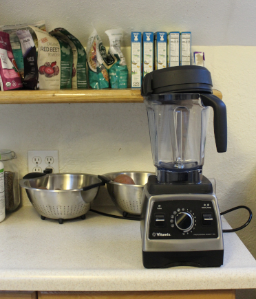 The photo shows a Vitamix blender atop my kitchen counter. In the background are various kitchen items, such as colanders and bags of quinoa.