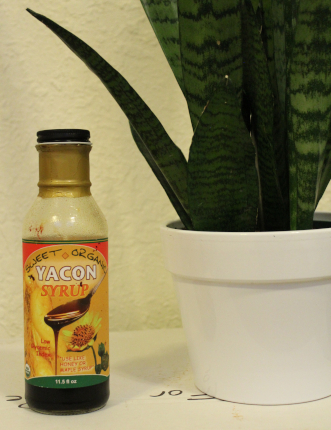 The photo shows a bottle of yacon syrup and, in a white pot, a snake plant