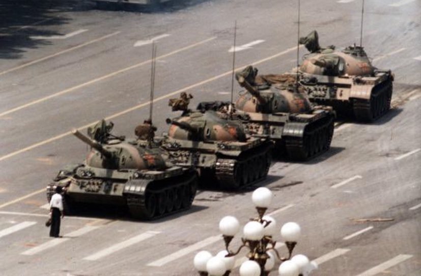 The image shows a man standing defiantly in front of a line of Chinese tanks