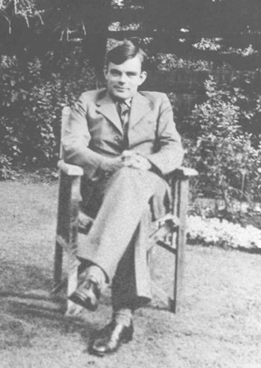 The black-and-white image shows Alan Turing sitting in a chair, a frontal photo