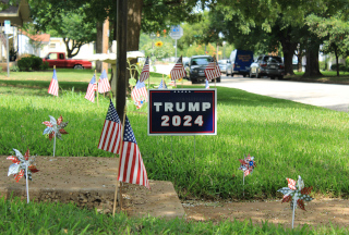 The color photo shows a grassy residental lawn with a Trump 2024 sign and US flags.