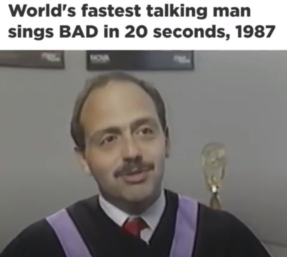 The image is a screenshot from a TV news segment. It shows John Moschitta Jr. in academic attire promoting his new ten-minute university spoof. Above, there's a caption saying: "World's fastest talking man sings bad in 20 seconds, 1987." It's a reference to the Michael Jackson song "Bad."