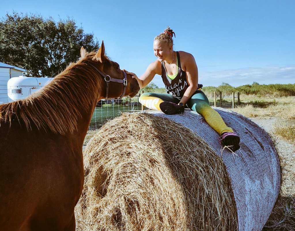 Photo shows Reality Winner sitting atop a bale of hay petting a large horse looking up at her.