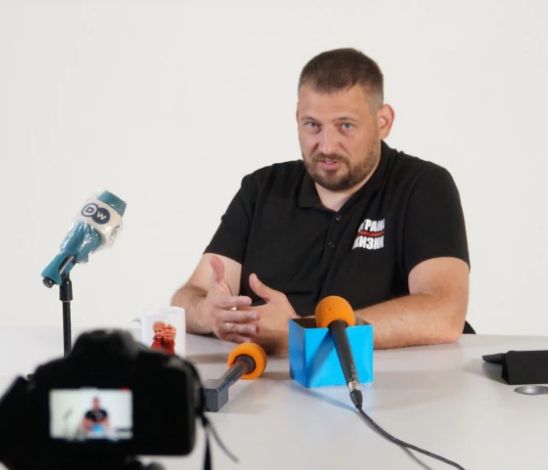 The podcaster sitting behind a desk with microphones etc.